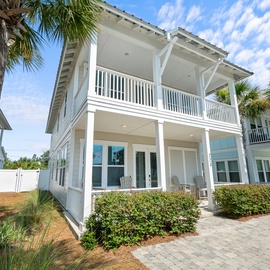 Elegant coastal home with covered balcony and tropical palm trees creating the perfect beach getaway atmosphere.