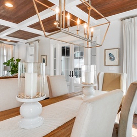 Gather around this elegant dining table under dramatic statement lighting, where memorable meals unfold in this sophisticated coastal-inspired space.