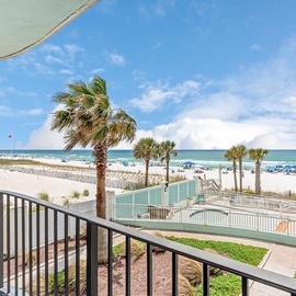 Beachfront balcony overlooking pristine white sand, swaying palms, and turquoise waters with colorful umbrellas dotting the shore.