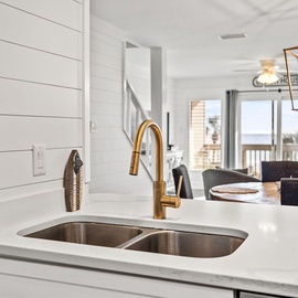 Your modern kitchen island beckons with gleaming brass fixtures and pristine counters, perfectly positioned for cooking while staying connected to your loved ones.