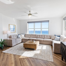 Unwind in your bright coastal living room where ocean views stretch beyond floor-to-ceiling windows and plush seating awaits your relaxation.