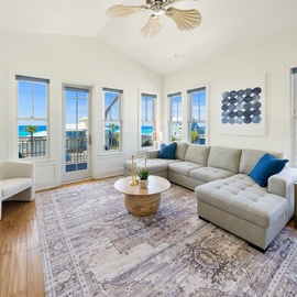 Relax in your bright living space with panoramic ocean views through floor-to-ceiling windows and a spacious sectional for ultimate comfort.