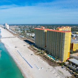 Beachfront resort towers rise along pristine white sand shores with turquoise waters stretching endlessly along the coastline.