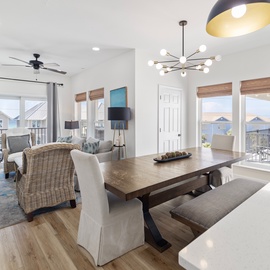 Step into your bright, open living space where coastal breezes flow through and sunlight pours in from every window, inviting you to unwind at the dining table or sink into comfortable seating with ocean views just beyond.