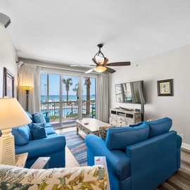 Unwind in your bright living room with vibrant blue seating, where stunning ocean views through floor-to-ceiling windows create the perfect backdrop for relaxation.
