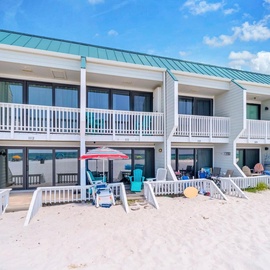 Your private beachfront patio leads directly onto soft white sand, where colorful beach chairs and your own umbrella await. Step inside to ocean views through floor-to-ceiling glass doors, or relax on the balcony above.