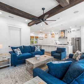 Relax in your stylish living space with plush blue seating and rustic wooden beams overhead, flowing seamlessly into a fully-equipped modern kitchen.