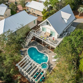 Aerial view of a coastal retreat featuring a private pool, spacious deck, and charming beach house architecture nestled among tropical foliage.