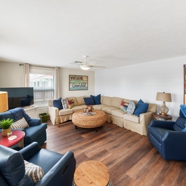 Gather with family in this spacious living room featuring comfortable seating, coastal artwork, and warm wood floors perfect for relaxing.