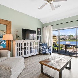 Unwind in your serene lakefront living room where soft blues meet warm comfort and stunning water views flow through floor-to-ceiling windows.