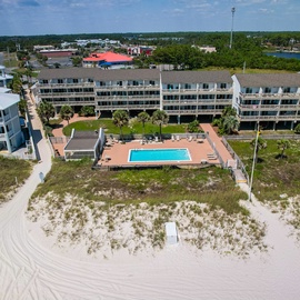 Beachfront property complex featuring multiple buildings with balconies, central pool area, and direct beach access along pristine sandy shores.