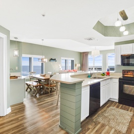 Step into your open-concept haven where coastal green hues and white cabinetry create the perfect space for preparing meals and gathering together.