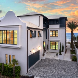 Stunning beachfront property featuring elegant architecture and tropical landscaping, perfectly positioned near the shore with dramatic sunset skies overhead.
