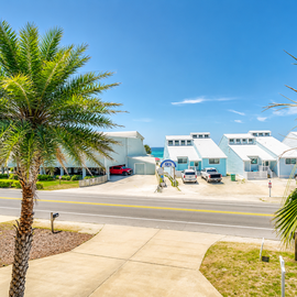 Modern coastal buildings with palm trees create a tropical neighborhood setting beneath clear blue skies.