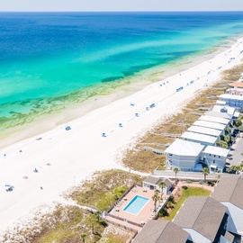 Stunning aerial view showcases pristine white sand beach with crystal-clear turquoise waters and beachfront vacation rentals.