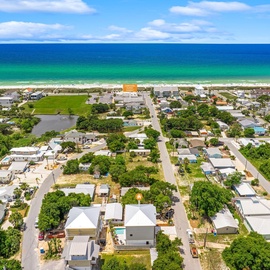 Aerial view of a charming beachfront community with tree-lined streets leading to pristine white sand beaches and turquoise waters.