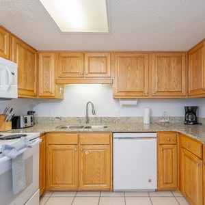 The fully-equipped kitchen features warm wood cabinetry, a breakfast bar with white stools, and granite countertops