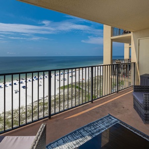 The balcony features wicker seating and offers a breathtaking view of the beach and tranquil waters beyond