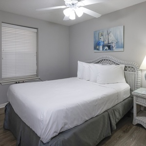 Cozy guest bedroom featuring a queen bed, light gray walls, and nautical decor, complemented by a small TV and bedside lamp