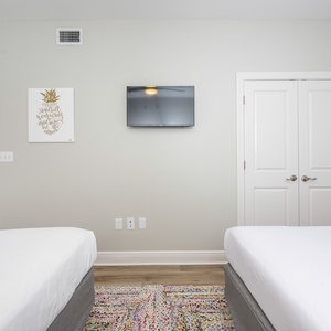 Guest bedroom featuring two queen beds, a wall-mounted TV, and colorful decor with a cozy area rug adding warmth to the space
