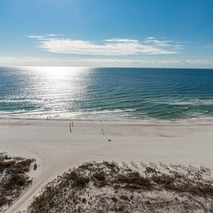 The image showcases a serene view of the beach with gentle waves lapping against the white sand under a clear blue sky