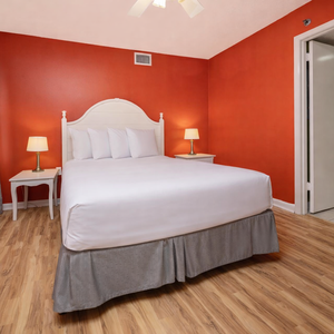 The vibrant red walls frame the guest bedroom featuring a queen bed, bedside lamps, and a view of a green-tinted bathroom