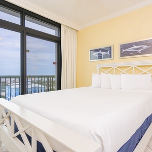 Bright and airy bedroom featuring a queen bed, coastal decor, and expansive views through the balcony doors