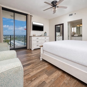 Cozy master bedroom featuring a king bed, light wood furnishings, and a sliding door leading to a balcony with a scenic view