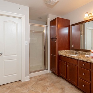 This bathroom features elegant dark wood cabinetry, a walk-in shower, and a granite countertop for a refreshing retreat