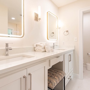 The master bath features a sleek double vanity with bright lighting, fresh towels, and a vanity stool for added comfort