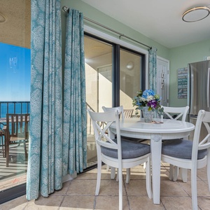 Dining area with a view of the tranquil sea, featuring a round table, stylish chairs, and stainless appliances nearby