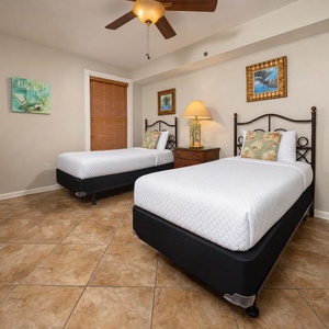 This guest bedroom features two cozy twin beds, warm wood accents, and beach-themed decor for a relaxing stay