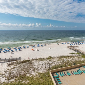 A vibrant beach scene features colorful umbrellas and sunbathers on soft white sand, with gentle waves lapping at the shore