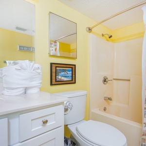 Bright guest bathroom featuring a tub/shower combo, white towels, and a cheerful yellow wall with beach decor