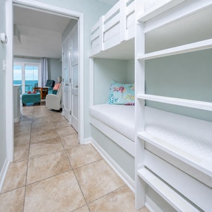 This cozy nook features built-in bunk beds with colorful pillows, leading to a bright living area with a beachfront view
