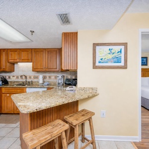 The kitchen features warm wood cabinetry, granite countertops, and a breakfast bar with two wooden stools