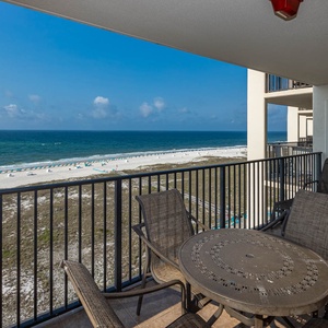Balcony overlooks the beach and pool area, with a view of white sand and turquoise chairs lining the shore under a clear sky