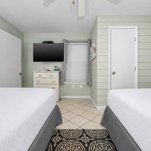 Guest bedroom featuring two queen beds, a mounted TV, and light green walls, creating a relaxing atmosphere for visitors