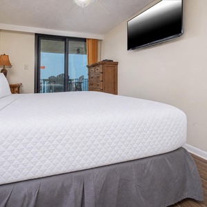 The master suite features a king bed, a wooden dresser, and the balcony door leading to a relaxing outdoor seating area