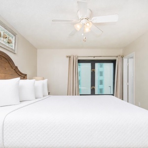 This bedroom features a plush king bed with crisp white linens and a serene view through large windows