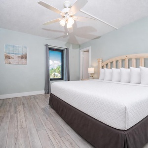 The master bedroom features a large bed, soft bedding, and a view of lush greenery through the window