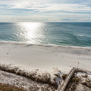 Serene beach with soft white sand, gentle waves, and a wooden walkway leading to the shore