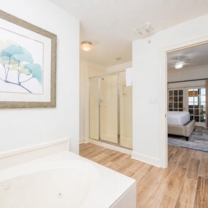 The master bath features a relaxing soaking tub, a glass walk-in shower, and a serene view into the cozy master suite