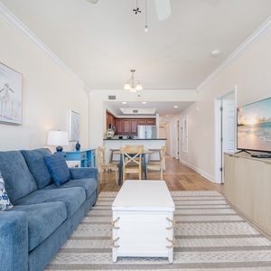 This inviting living area features a comfortable blue sofa, a large TV, and a view of the kitchen with warm wood cabinetry