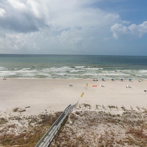 Expansive view of the beach front with white sand, lounge chairs, and gentle waves under a blue sky