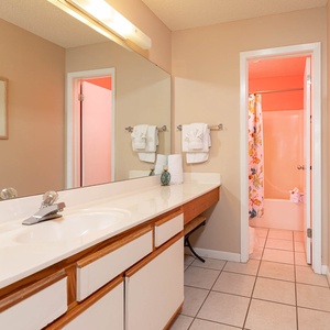 The master bathroom features a spacious countertop with a large mirror, colorful shower curtain, and a tub/shower combo