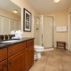 The extra bath features a granite countertop, a glass walk-in shower, wooden cabinetry, and laundry closet with washer/dryer