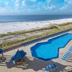 The inviting pool area features a vibrant blue pool surrounded by lounge chairs and shaded seating, with a view of the beach