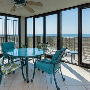The enclosed balcony area features a round table and patterned chairs, offering a serene view of the gulf