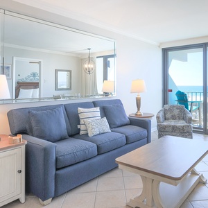 The living area features a plush sofa and a stunning beachfront view from the sliding glass doors